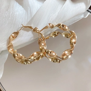 Détail de boucles d'oreilles créoles torsadées dorées avec finition brillante et tige en argent