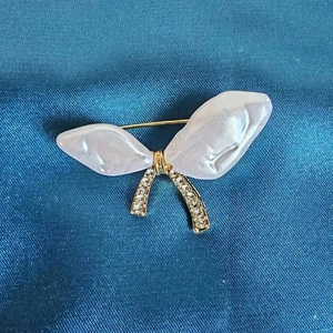Macro detail of a golden bow brooch with white resin wings and sparkling rhinestones