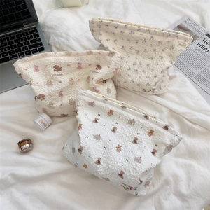 Three quilted makeup bags featuring floral and bear patterns on a soft white bed