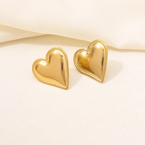 Close-up of polished 18K gold plated heart stud earrings on soft fabric background
