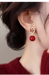 Détail de boucles d'oreilles rose rouge dorées avec perles portées par un mannequin