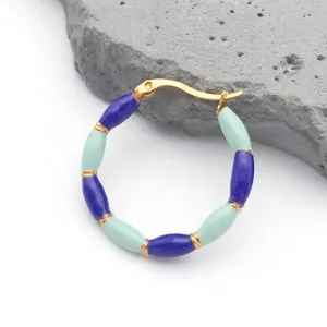 Detail of gold bamboo-style earrings with blue and mint green enamel beads on a grey rock