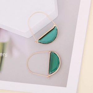 Chic gold-framed emerald green glass crescent earrings displayed on geometric props