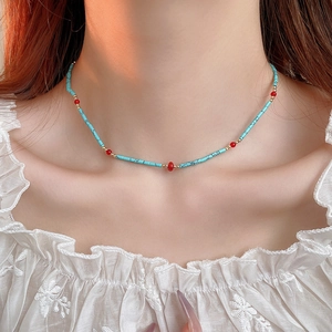 Detail of bohemian turquoise beaded necklace with red accents on model's neckline