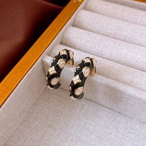 Detail view of C-shaped black enamel hoop earrings with gold clover floral patterns