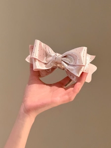 Detail of pink polka dot satin bow hair clip held in hand against brown background