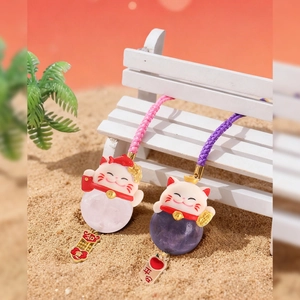 Lucky cat crystal bag charms in pink and purple quartz on a mini bench with beach background