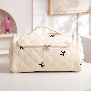 Detail of cream quilted makeup bag with black bow embroidery and dual zippers