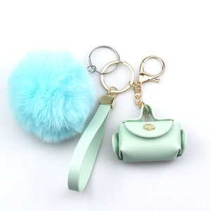 Detail of light blue pompom and green leather mini bag keychain with wrist strap