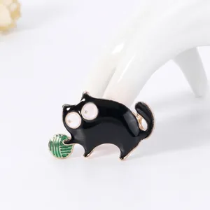 Macro shot of black enamel cat brooch with green ball detail on a white display hand