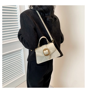 Detail view of cream textured leather crossbody bag with bold gold buckle on black suit