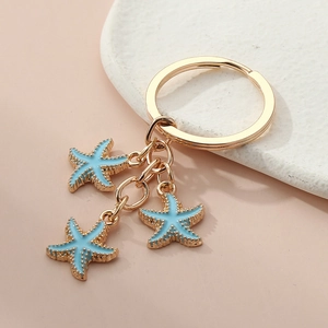 Detail of three blue starfish charms on a gold keychain with textured enamel finish