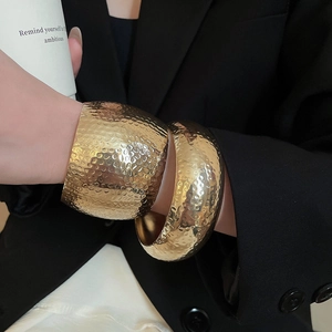 Detail of wide golden textured bangles with hammered finish worn on model's wrist