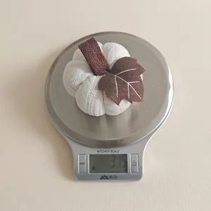Detailed view of a white knitted pumpkin ornament showing 31.5g weight on a kitchen scale