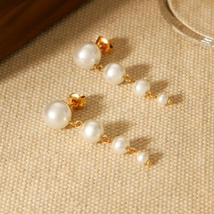 French pearl drop earrings in 18k gold plated stainless steel on a beige textured fabric