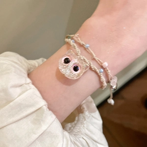 Close-up of a pink champagne woven bracelet with a cute cat charm on a woman's wrist