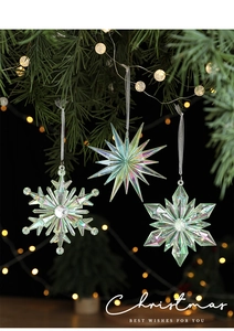 Detail of iridescent acrylic snowflake and star ornaments hanging on a green Xmas tree