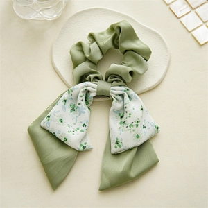 Close-up of green floral bow hair tie on a white ceramic plate with soft lighting