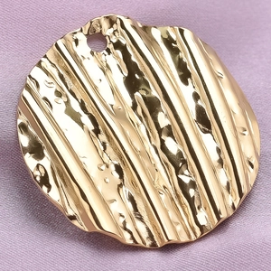 Macro shot of gold stainless steel circular pendant with unique wavy hammered texture