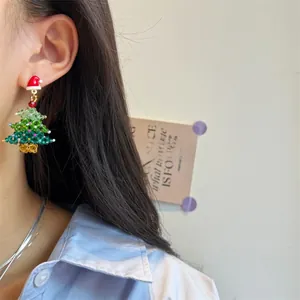 Detail of handmade beaded Christmas tree earrings with a red hat on a female model