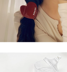 Detail showing a red heart hair claw with pearls worn on hair and a glass storage jar
