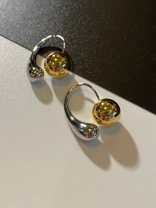 Detail of two-tone C-shaped earrings with gold metal sphere and silver waterdrop design