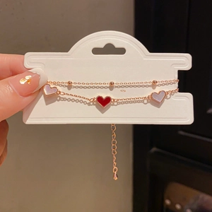 Detail of rose gold double-layer heart bracelet with red enamel and white shell charms