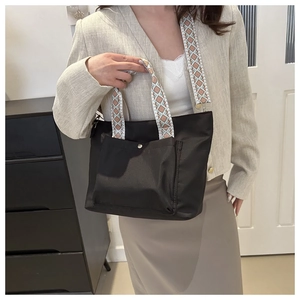 Detail of black fabric tote bag with geometric wide strap and functional front snap pocket