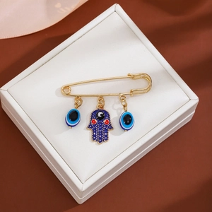 Detail of gold brooch with blue evil eye charms and Hamsa hand on white jewelry cushion
