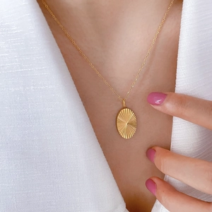 Detail shot of a 18K gold plated oval pendant featuring sunburst texture on a model neck