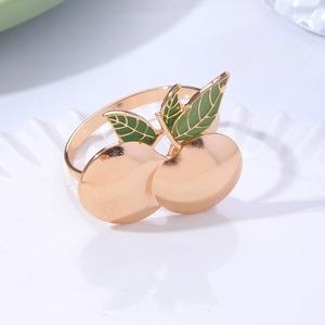 Macro detail of gold metal napkin ring with green enamel leaf and cherry fruit shape