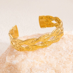 Detailed view of golden textured bangle with woven design on natural stone prop