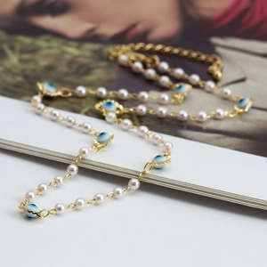 Evil Eye pearl necklace with gold chain and blue beads over a stylish magazine backdrop