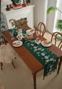 Detail of dark green Christmas table runner featuring festive ornaments and gold tassels