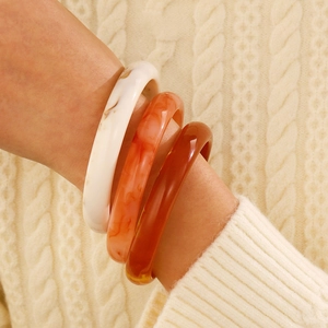 Close-up of three marbled acrylic bangles worn on a wrist over a knit sweater