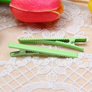 Macro detail of two light green metal duckbill hair clips with non-slip serrated design