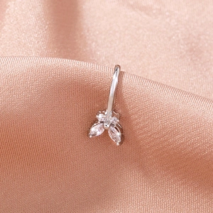 Macro shot of silver stainless steel piercing with three marquise-cut clear zircons on pink silk