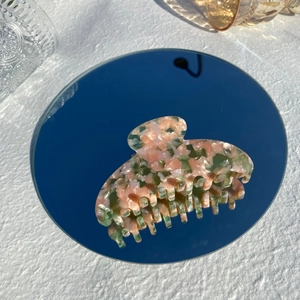 Close-up of pink and green marbled acetate hair claw clip reflected on blue mirror