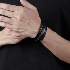 Close-up of black multilayer braided leather bracelet with metal feather charm on wrist
