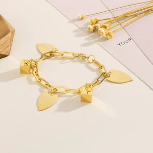 Close-up of golden geometric chain bracelet with cube and leaf pendants on a warm background