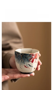 Close-up of hand holding a ceramic teacup with painted koi fish and gold accents