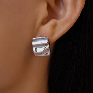 Close-up of silver square ripple stud earring with liquid metal texture on ear