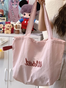 Pink drawstring canvas tote bag featuring artistic red lettering in a handheld lifestyle shot