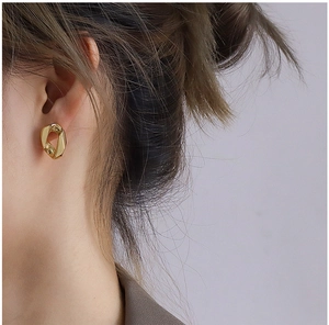 Gros plan d'un mannequin portant une boucle d'oreille ovale torsadée dorée minimaliste