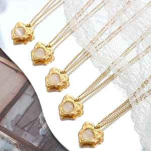 Gold heart necklaces with cat's eye stone pendants on reflective surface with lace