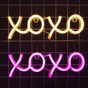 XOXO LED neon sign in warm yellow and pink light on a black mesh wall background