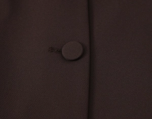Detailed macro view of matching fabric-covered button on dark brown straight-leg trousers