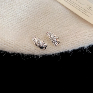 Macro shot of silver twisted hoop earrings with crystals on beige knit fabric