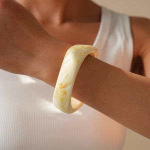 Macro detail of wide resin marble bangle with amber swirls on a model's wrist