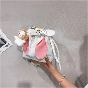 White canvas bucket bag with rabbit ears and cute charms shown held against a grey wall